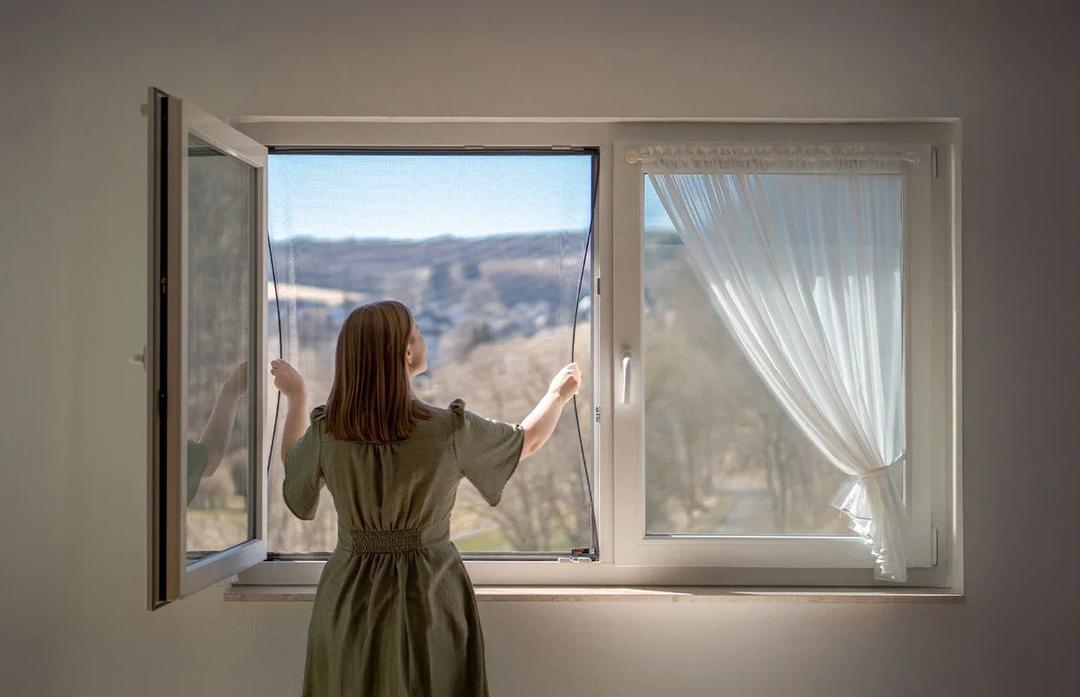 Frau öffnet flexiblen FlexScreen-Rahmen, der sich passgenau an das Fenster anpasst